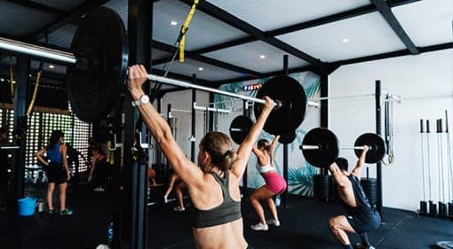a class of gym goers lifting barbells in barbell club