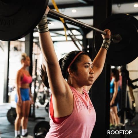 girl powerlifting barbell overhead in gym